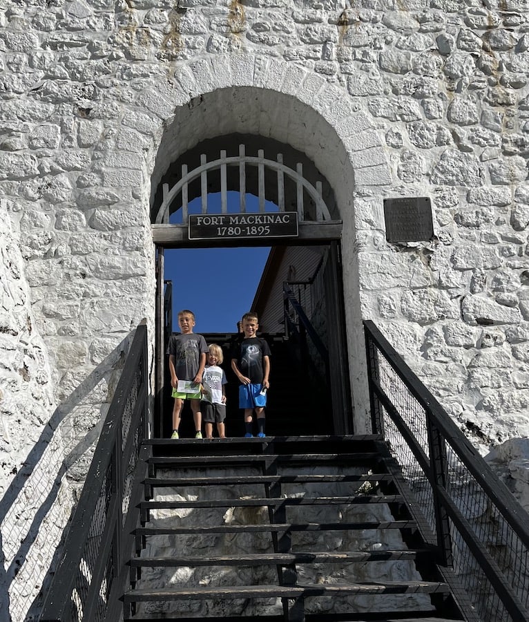 Three boys standing on the top of the stairs right under the arched entrance to Fort Mackinac on Mackinac Island.
