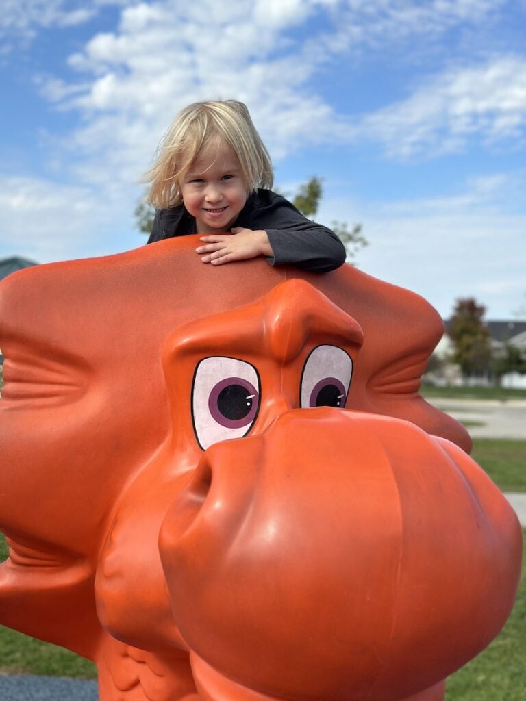 Boy on the top of an orange dragon's head at a playground