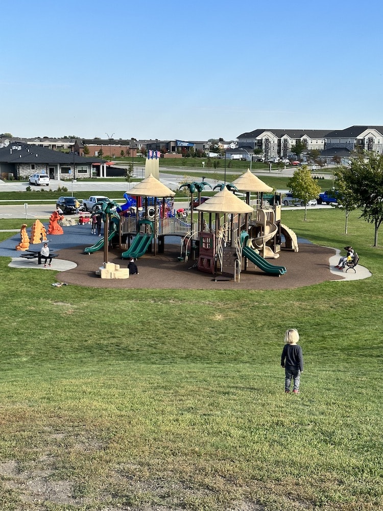 View from the top of a grassy hill looking down at two playgrounds