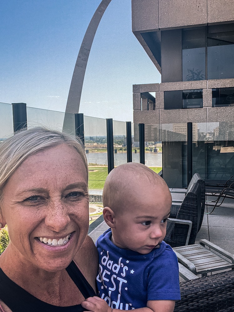 Mom and baby on the terrace of the Drury Plaza Hotel at the Arch with the Arch in the background.