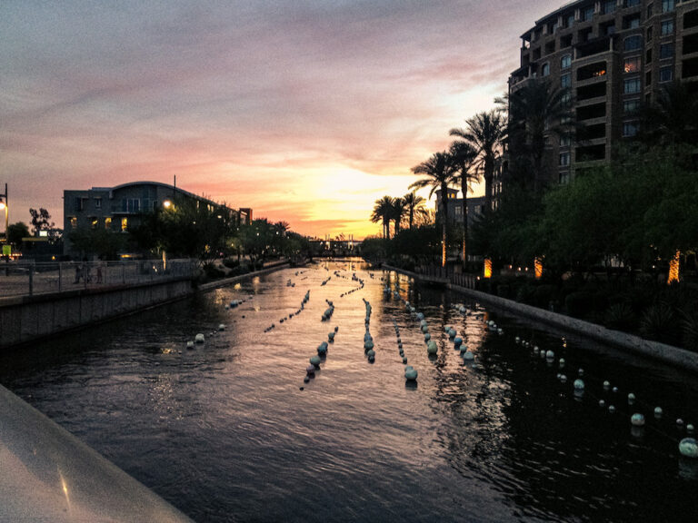 Sunset over the Scottsdale Waterfront canal near Old Town with palm trees, walkways, and city buildings