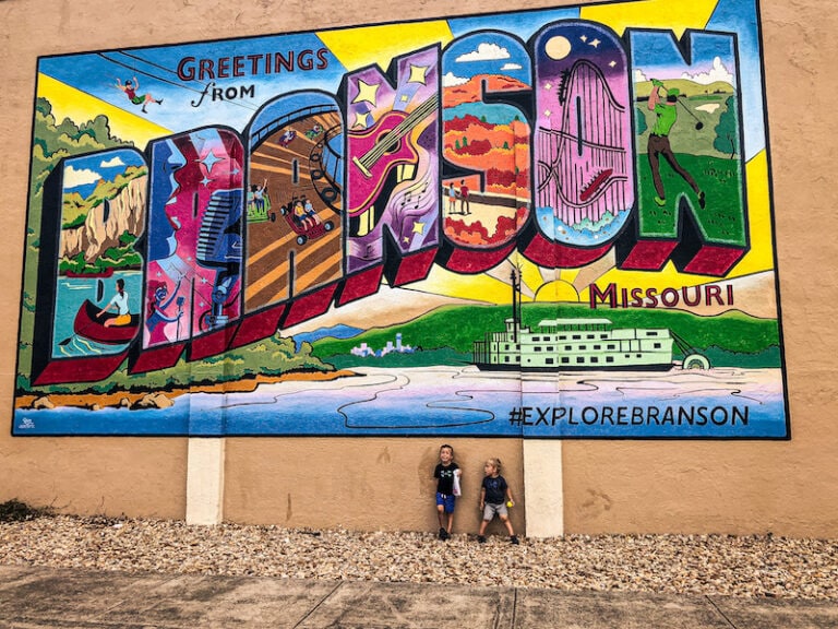 Boys standing in front of a large colorful 'Greetings from Branson' mural painted on the side of a building.
