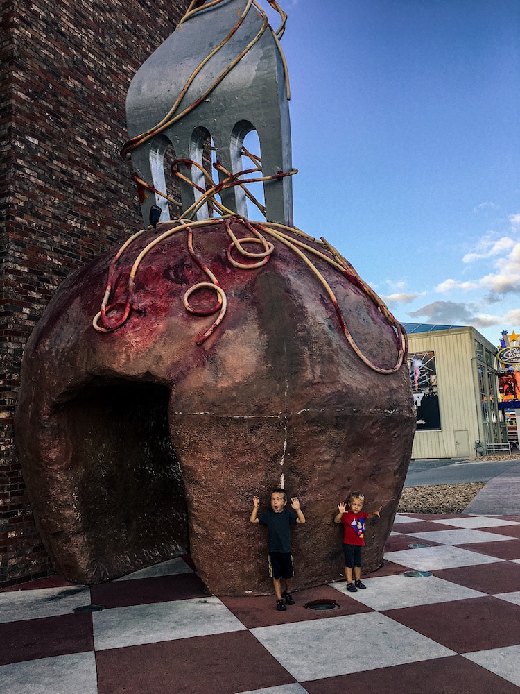Humongous meatball sculpture with a fork in it and two young boys standing in front of it.