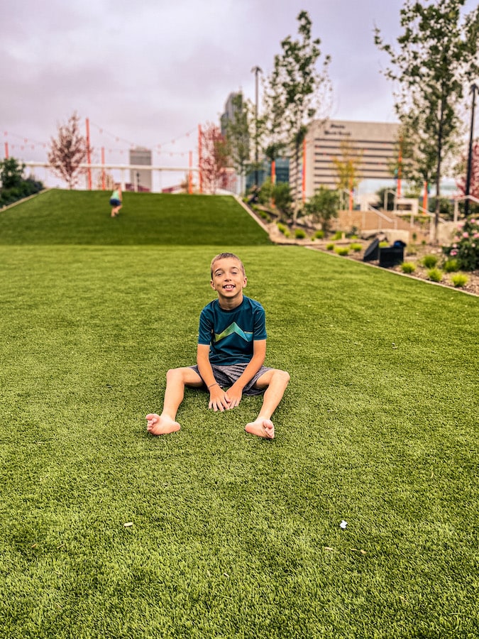 Boy sitting that the bottom of a large turf hill at the Gene Leahy Mall in downtown Omaha.