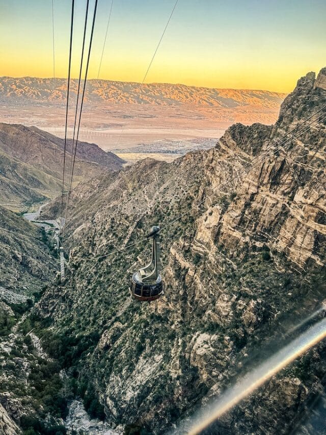 The Palm Springs Aerial Tramway tramcar connected to cables going down a large canyon with a colorful sunset in the background.