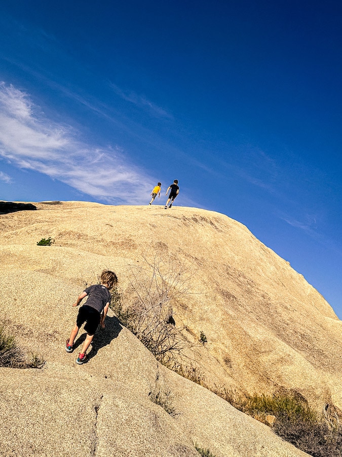 Three boys hiking up some enormous boulders