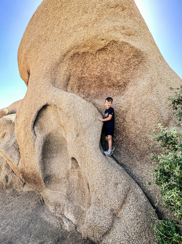 Boy standing near the "eye" of a rock shaped like a Skull