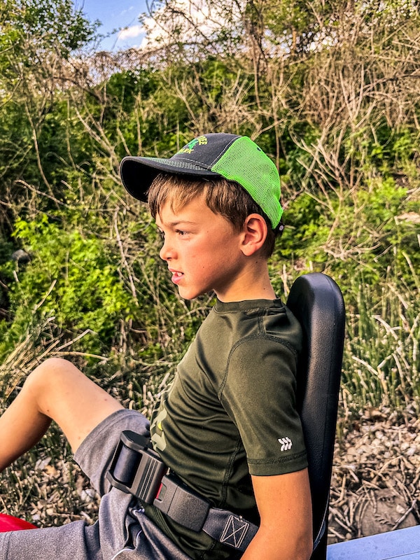 Boy with a green and gray hat on sitting on a rail bike with his seat belt on