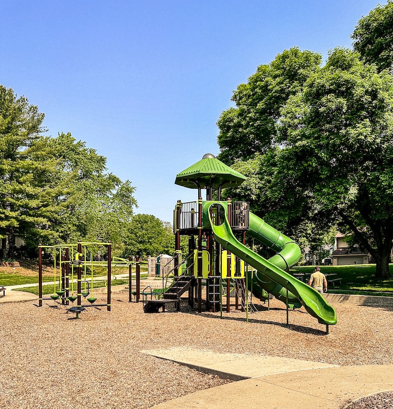 Green and brown colored playground with large open slide plus a large tube slide and other obstacles