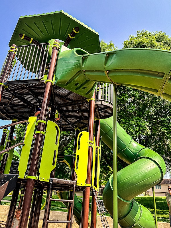 Close up view of green and brown playground with the tall green open slide and the tube slide