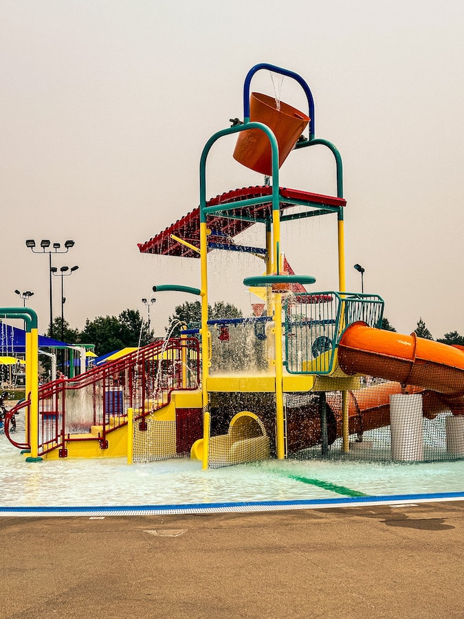 Water play structure with an orange tube slide and a red water bucket plus other sprayers and slides at Valley View Aquatic Center.