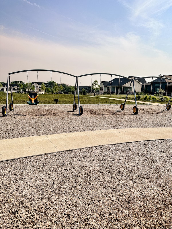 A variety of swings that have wheels at the bottom of the poles holding up the swings.