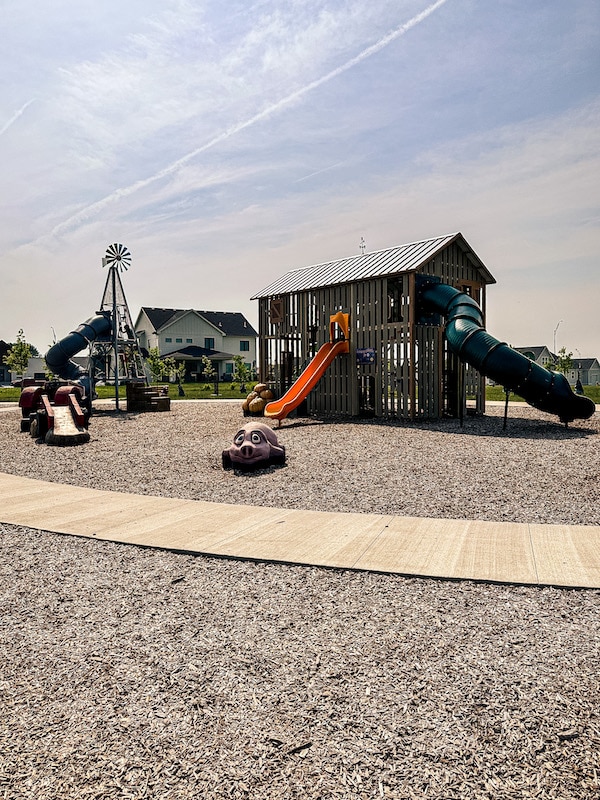 View of a playground shaped like a barn with a slide plus a pretend pig, tractor, and large separate slide shaped like a windmill.