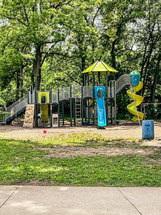 Neon green and blue playground for older kids with a couple of slides and a climbing wall. The playground is surrounded by trees