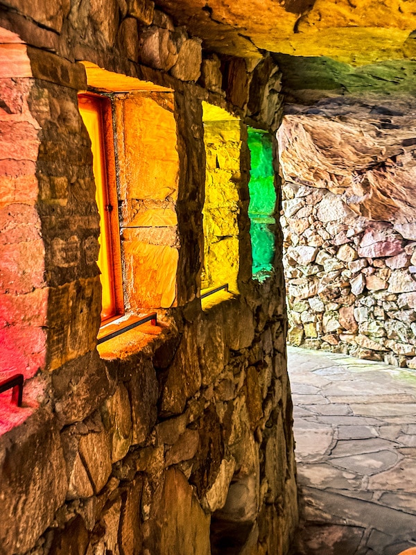 Square windows that are red, orange, yellow, and green through a tunnel surrounded by rocks