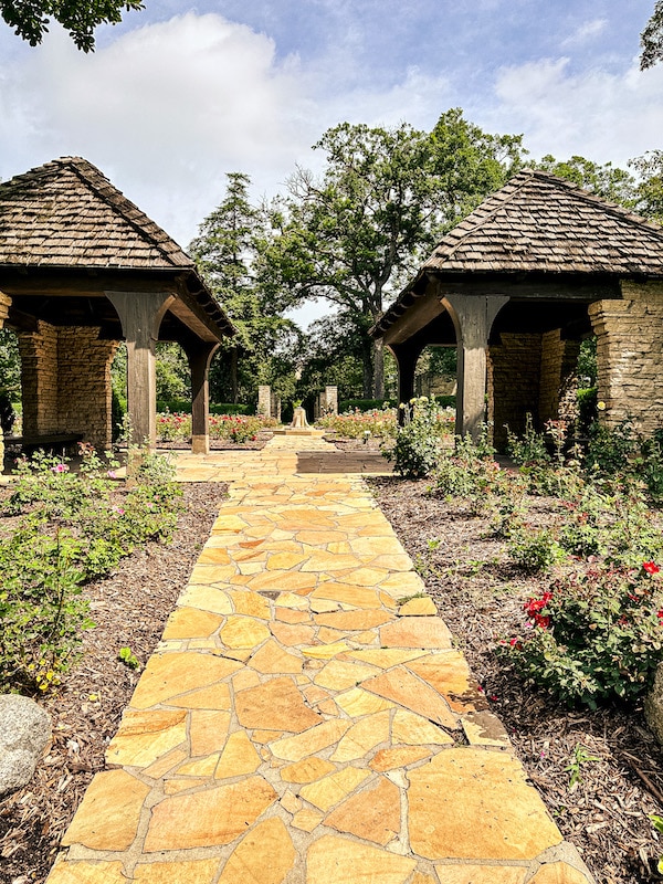 Two shelters across from each other with a stone walkway in between at the Clare and Miles Mills Rose Garden in Greenwood Park in Des Moines.