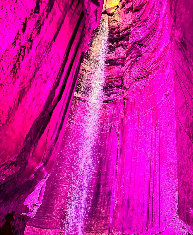 Waterfall in a cave that has pink lights highlighting the entire cave
