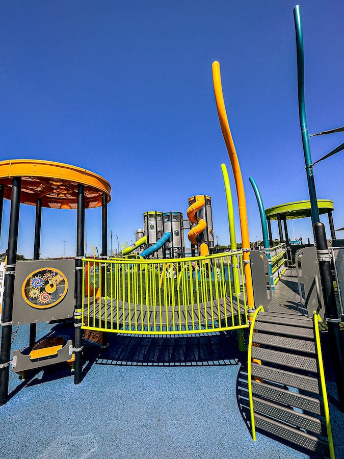 Green, orange, and gray playground with a small bridge for little kids to walk across
