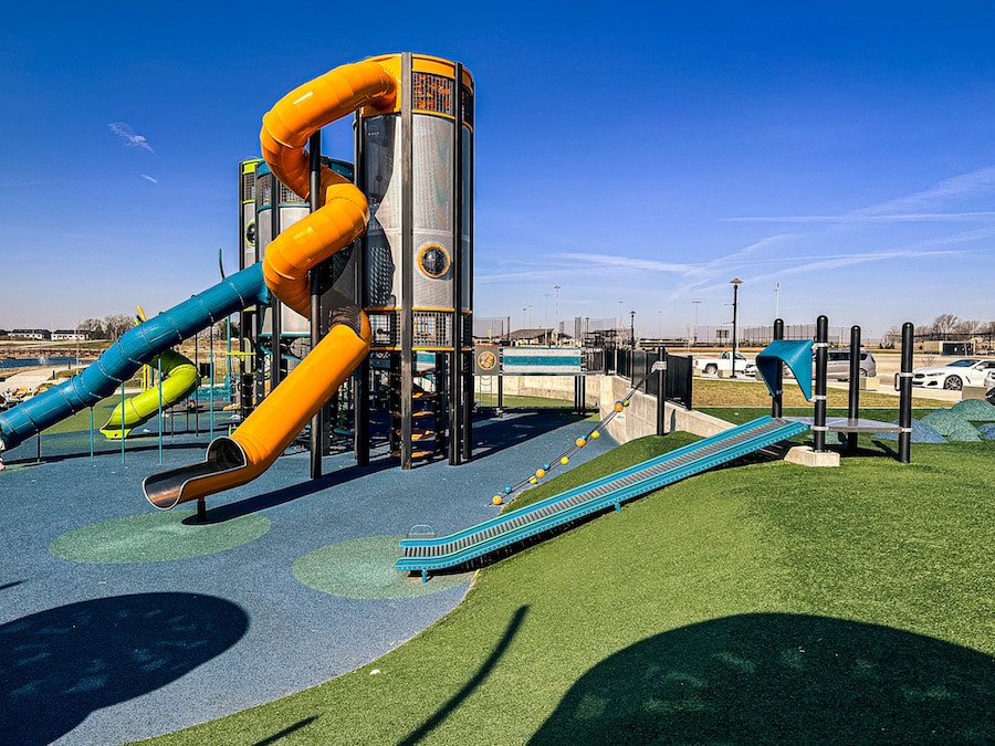 Tall orange tube slide along with a roller slide built into the side of a hill made of turf