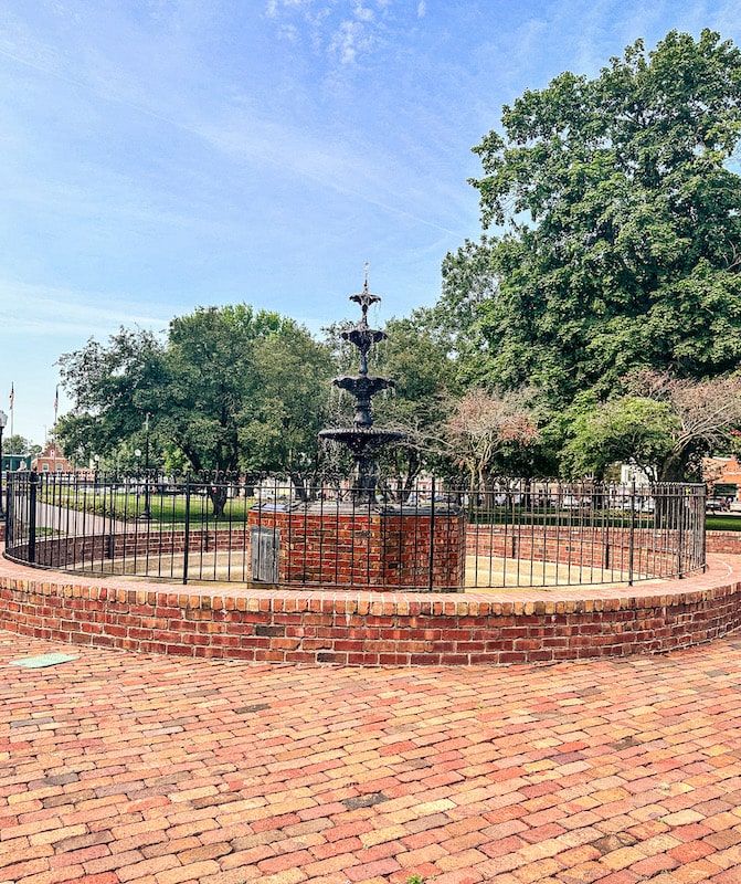 Fountain surrounding by a black fence and bricks in Central Park in Pella