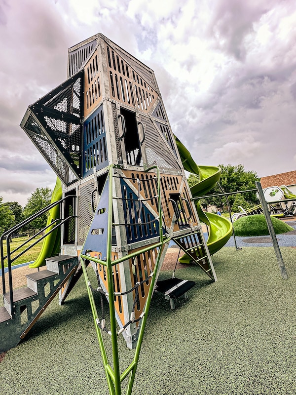 Tall brown play structure that is made up of triangular shapes and is covered.
