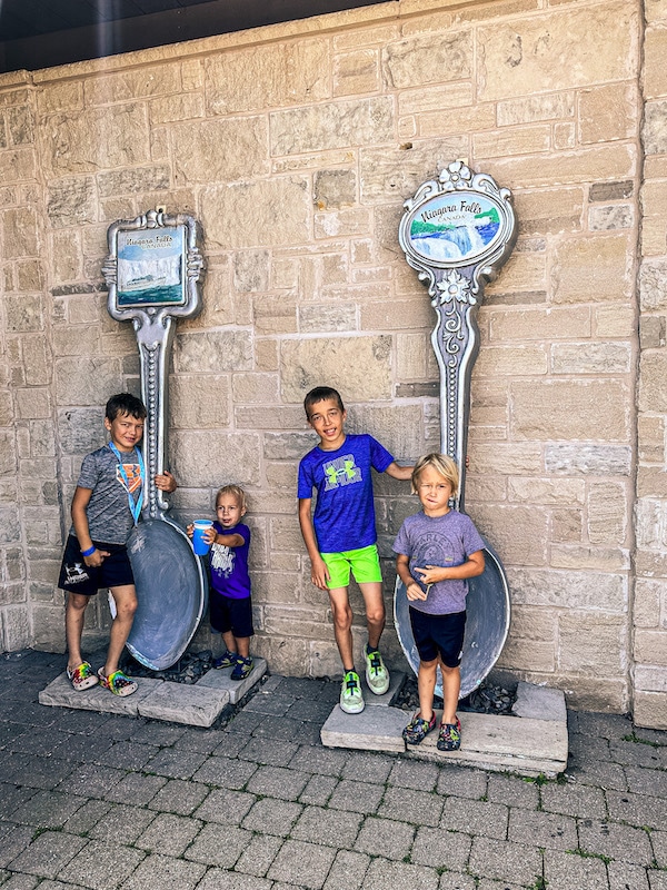Four boys standing next to two large Niagara Falls spoons.