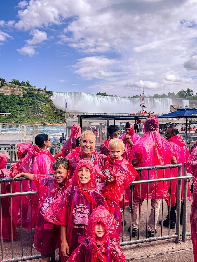 Family posing on the Niagara City Cruises dock wearing their red ponchos with American Falls in the background.
