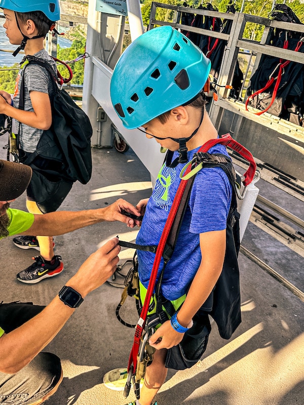 Boy wearing a teal helmet getting his harness on for ziplining.