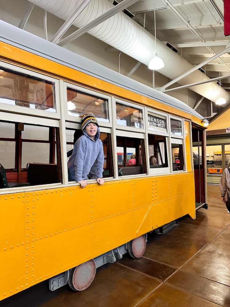 Boy wearing a stocking hat leaning out the window of a yellow trolley inside of the Durham Museum in Omaha.