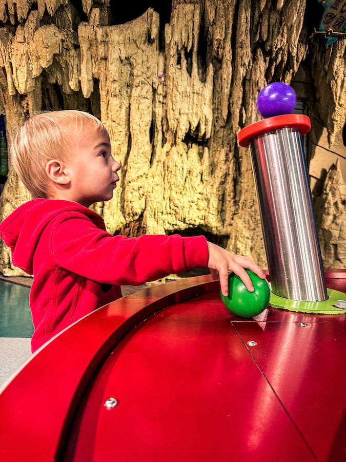 Boy wearing a red sweatshirt putting plastic balls on stucture blowing air at the Omaha Children's Museum.