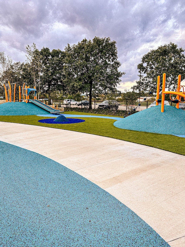 View of the two different rubber ground surface areas. One with an orange climbing structure and the other with a roller slide going down.