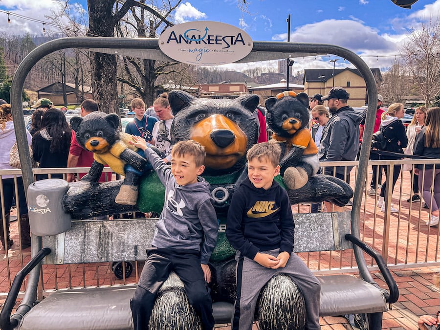 Boys sitting on the Anakeesta chondola with bear statues behind them.