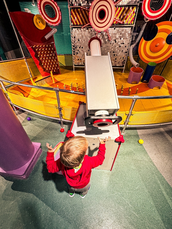 A young boy is putting a plastic ball into a ball shooter at the Omaha Children's Museum