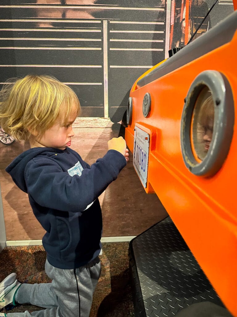 A young boy is working on the front of a pretend orange car at the Omaha Children's Museum.