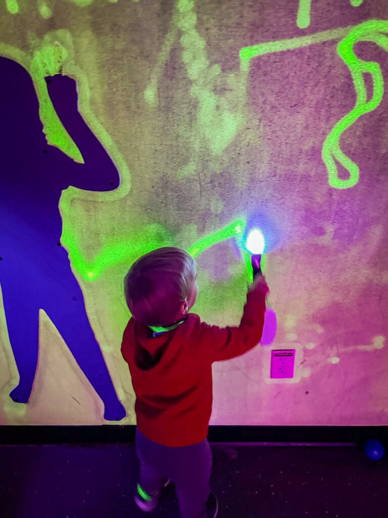 Young child using a flash light to make a drawing on a wall.