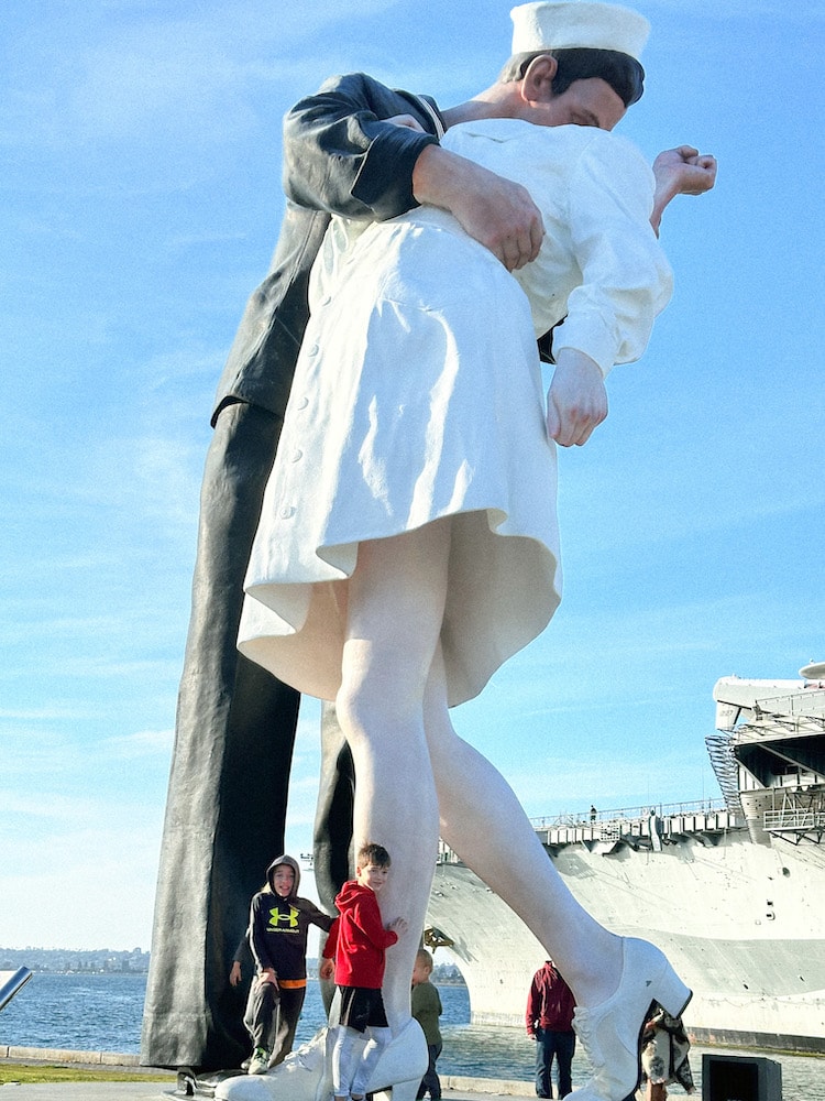 Close up view of the Embracing Peace sculpture which is a sailor and nurse embracing with a kiss. Three boys standing at the bottom of this sculpture posing for a picture.