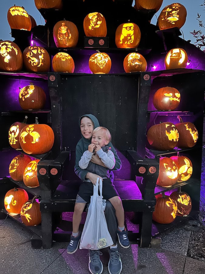 Two young boys sitting on a pumpkin throne surrounded by glowing, intricately carved jack-o’-lanterns at Spirits in the Gardens at Reiman Gardens in Ames, Iowa.