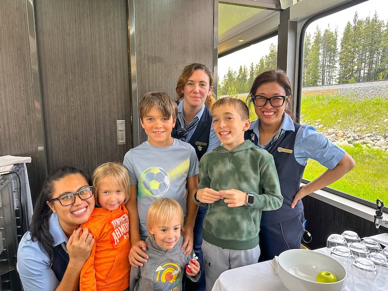 Four boys posing with three female Rocky Mountaineer staff members inside of the train.