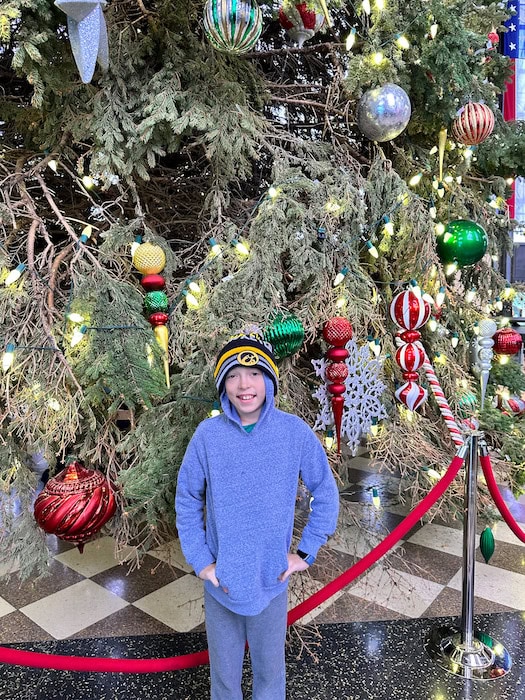 Boy wearing a sweatshirt and stocking hat standing in front of the decorated Christmas tree at the Durham Museum in Union Station in Omaha.