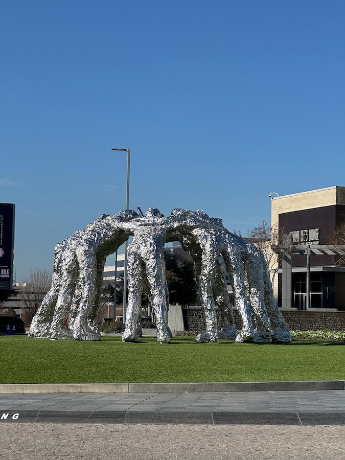 Crinkled looking football player huddle stainless steel statue in the center of a roundabout at the Star in Frisco, Texas.