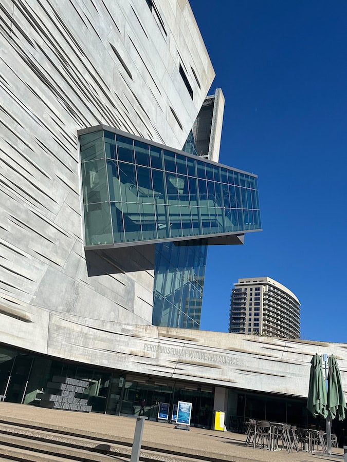 The exterior view of the Perot Museum of Nature and Science that looks like a geological formation and has a glass escalator that extends diagonally from the building.