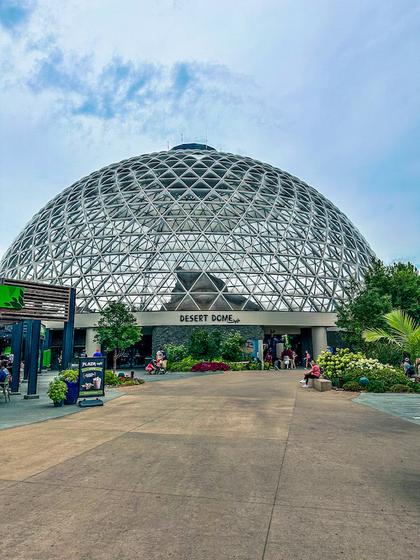 Exterior view of the Desert Dome at Omaha’s Henry Doorly Zoo, featuring its large glass dome-shaped structure and the entrance with visitors walking nearby.
