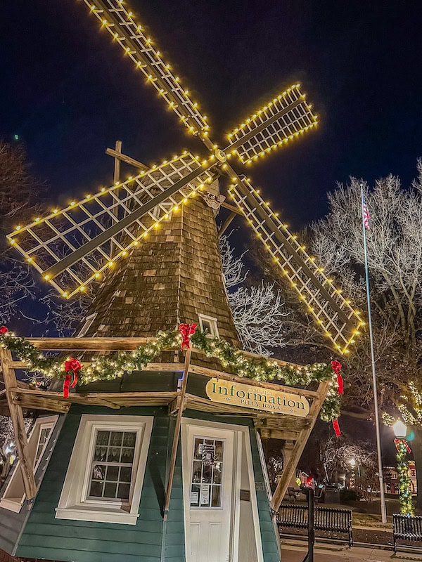 Pella, Iowa Visitor Information Center shaped like a traditional Dutch windmill, decorated with Christmas garlands, bows, and twinkling lights against a dark winter night sky.
