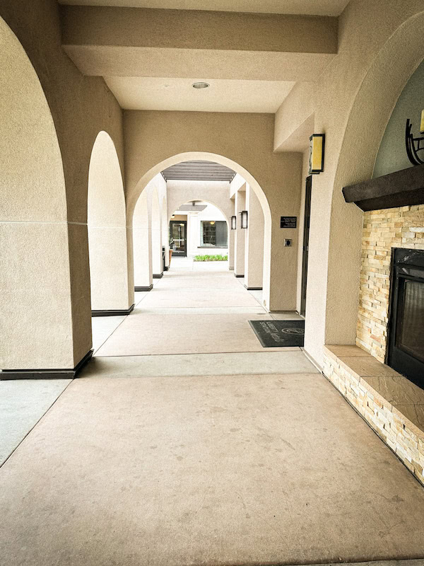 Covered outdoor corridor at Homewood Suites Liberty Station with cream stucco arches and a stone fireplace.