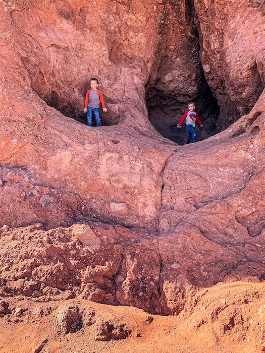 Two boys stand inside two red-rock openings at Hole-in-the-Rock in Papago Park, Phoenix, during a sunny family hike.