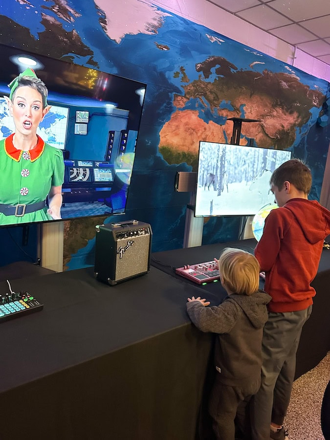 Kids interacting with Santa’s Command Center at the Holiday Hullabaloo in Des Moines, featuring festive screens and immersive holiday displays.
