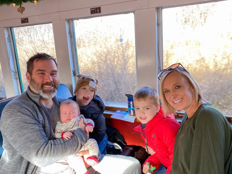Family riding the Santa Express train in Boone, Iowa, smiling together in a decorated train car during the holiday season.