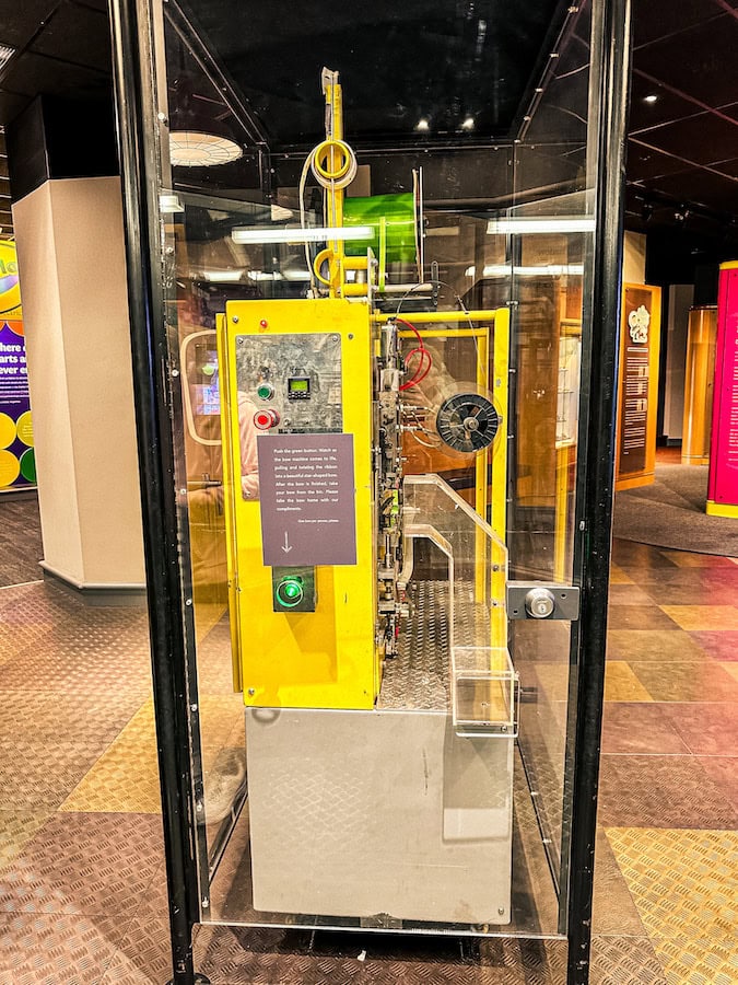 Close-up of the bright yellow bow-making machine at the Hallmark Visitors Center in Kansas City, where visitors can press a green button to watch ribbons twist into a perfect bow.
