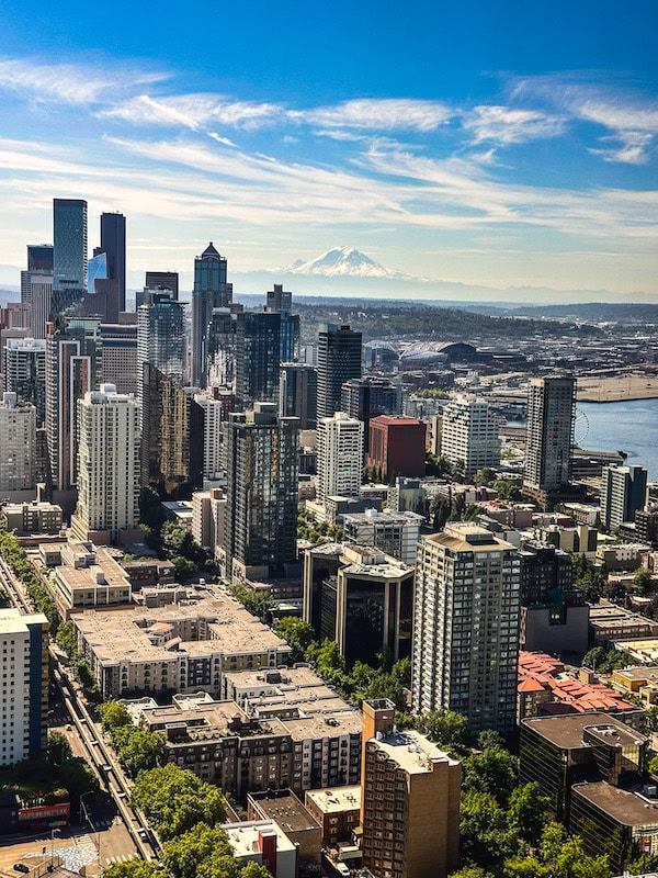 Aerial view of downtown Seattle skyscrapers with Mount Rainier visible in the distance on a clear day, taken from the Space Needle.