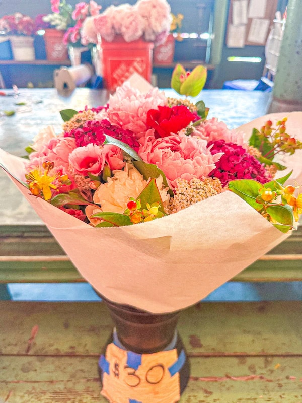 A colorful bouquet of fresh flowers wrapped in white paper and displayed in a vase at Pike Place Market, with additional flowers blurred in the background.